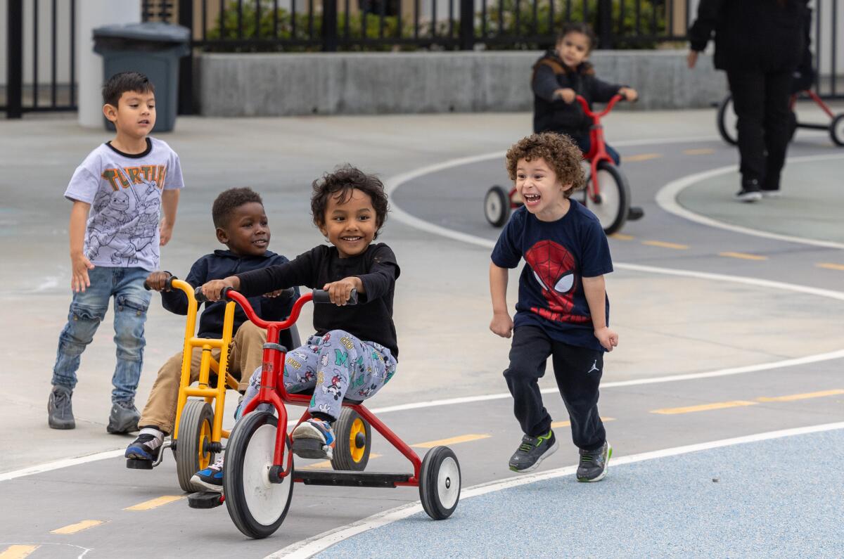 Students ride tricycles on a playground.