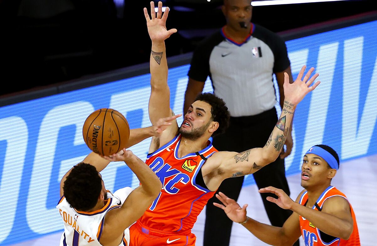 Phoenix Suns' Devin Booker, left, tries to shoot past Oklahoma City Thunder's Abdel Nader, center, during the first half of an NBA basketball game Monday, Aug. 10, 2020, in Lake Buena Vista, Fla. (Mike Ehrmann/Pool Photo via AP)