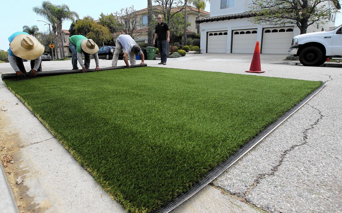 Workers on a turf removal and replacement job install artificial grass at a Pacific Palisades home.