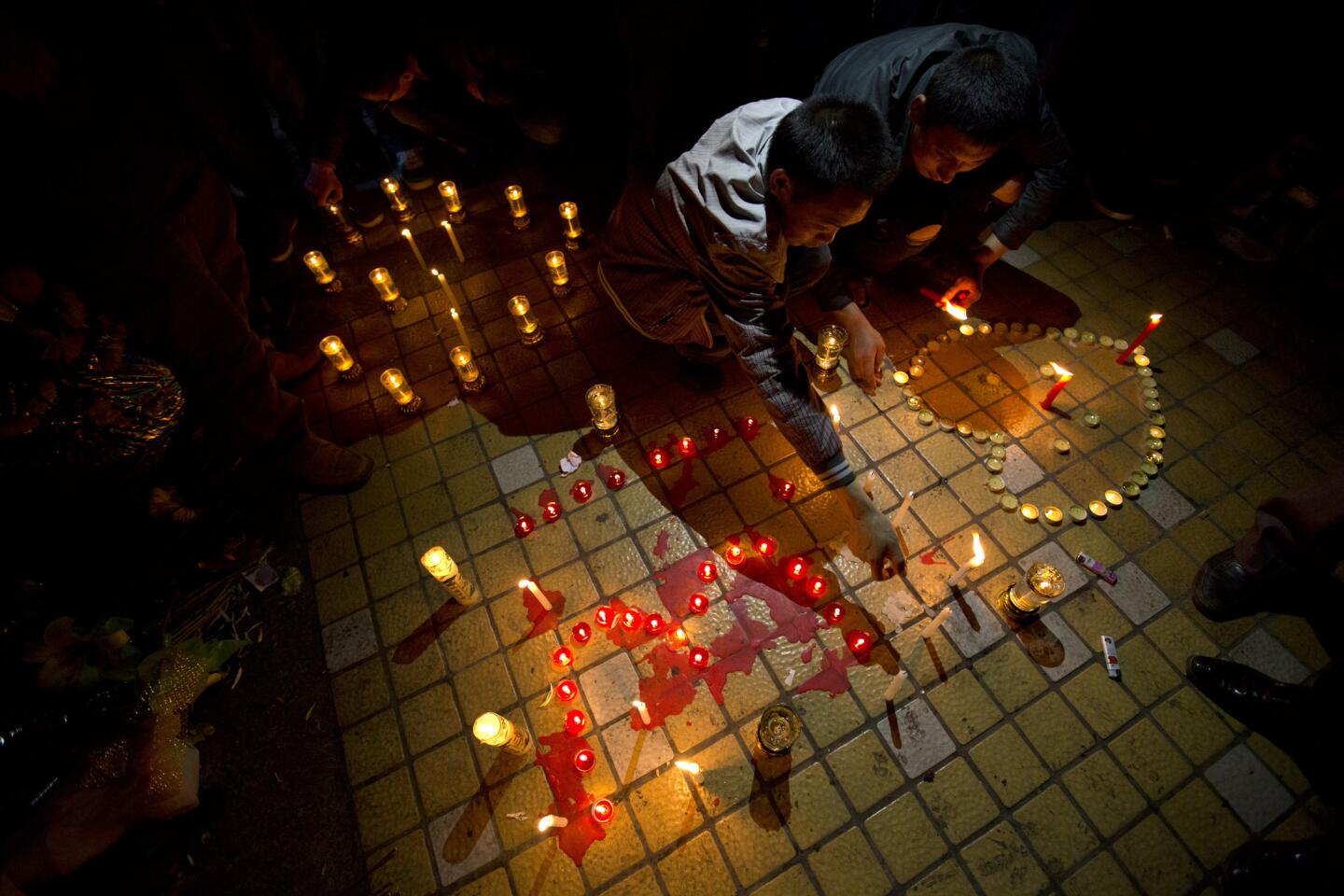 Two men light candles before a group prayer for the victims on a square outside the Kunming Railway Station where assailants slashed scores of people with knives the night before.
