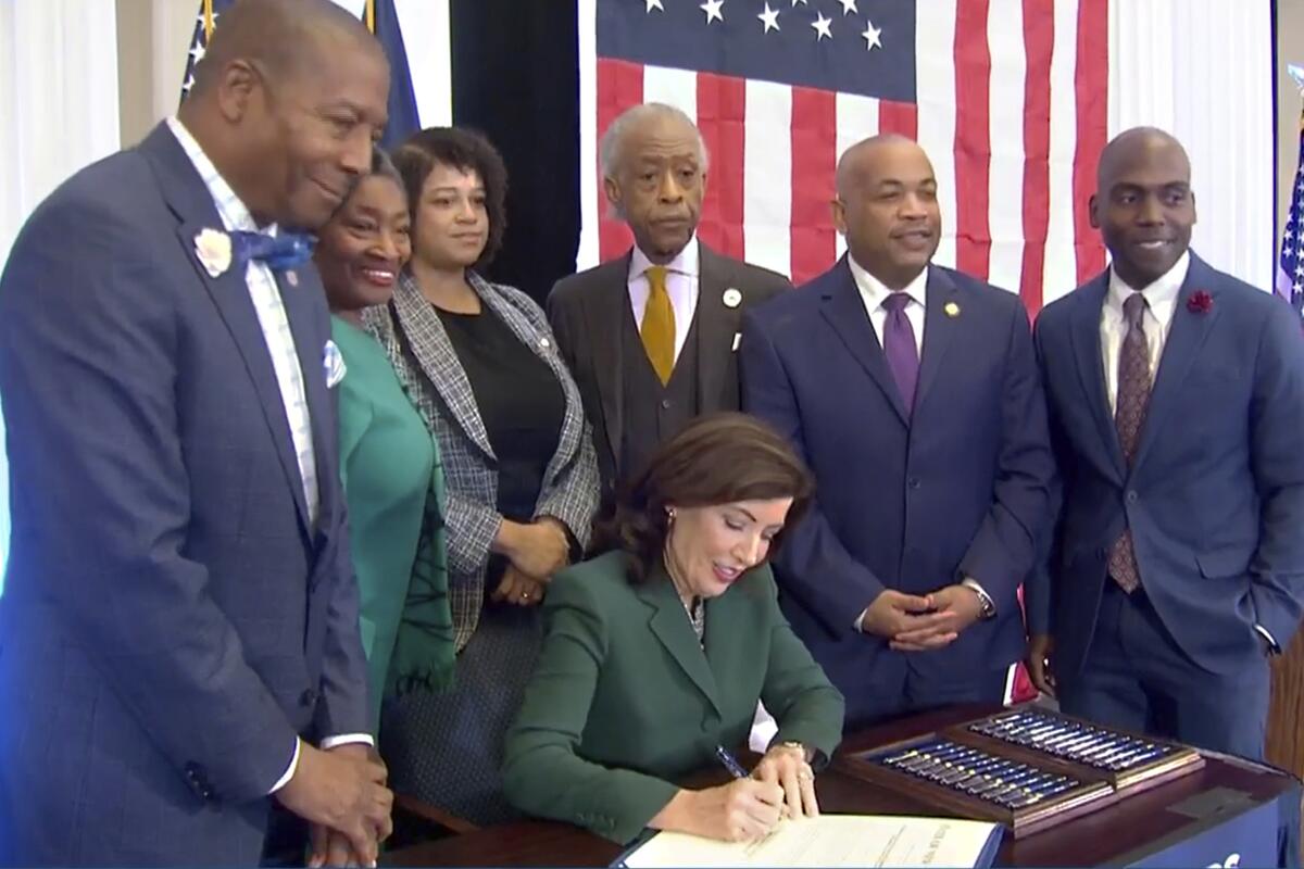 New York Gov. Kathy Hochul signs a bill as people watch.