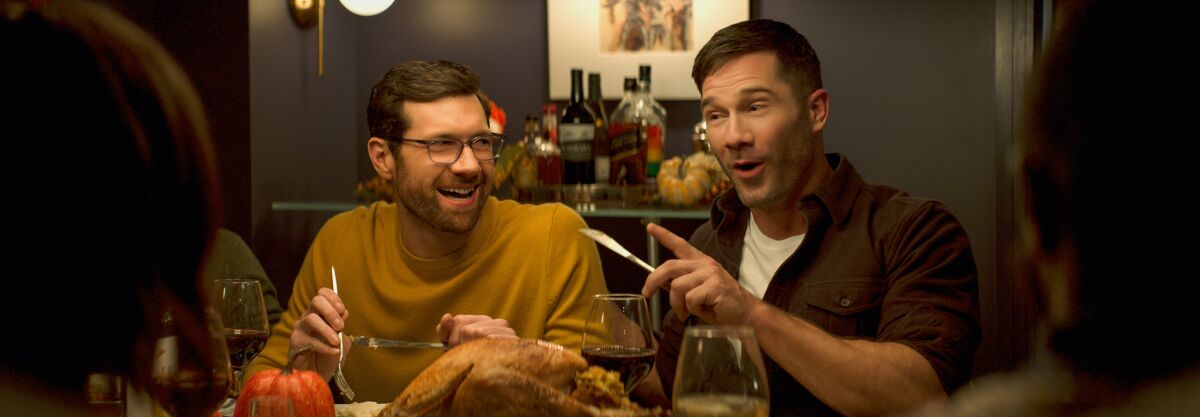 Two men at a holiday dinner table in the movie "Bros."