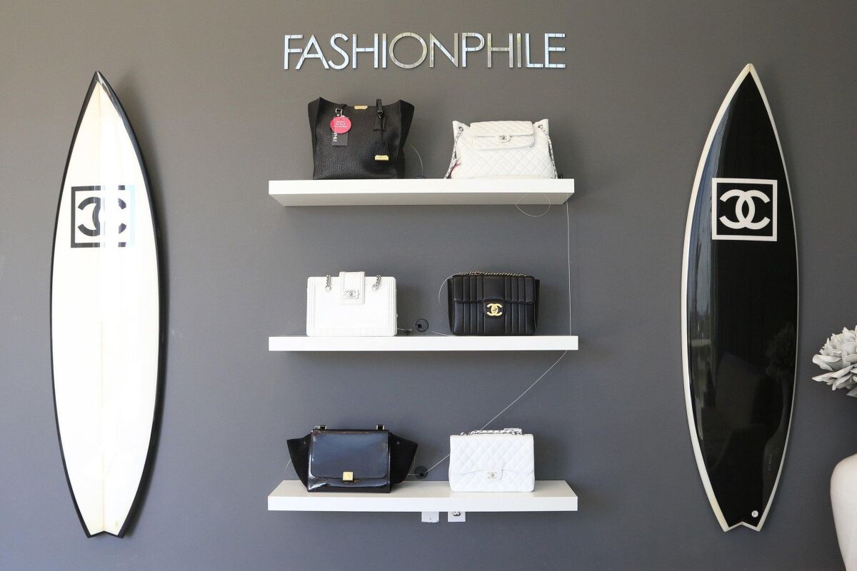 A wall in the Fashionphile showroom in Carlsbad features one-of-a-kind Chanel surfboards, mounted next to an array of luxury handbags. — David Brooks