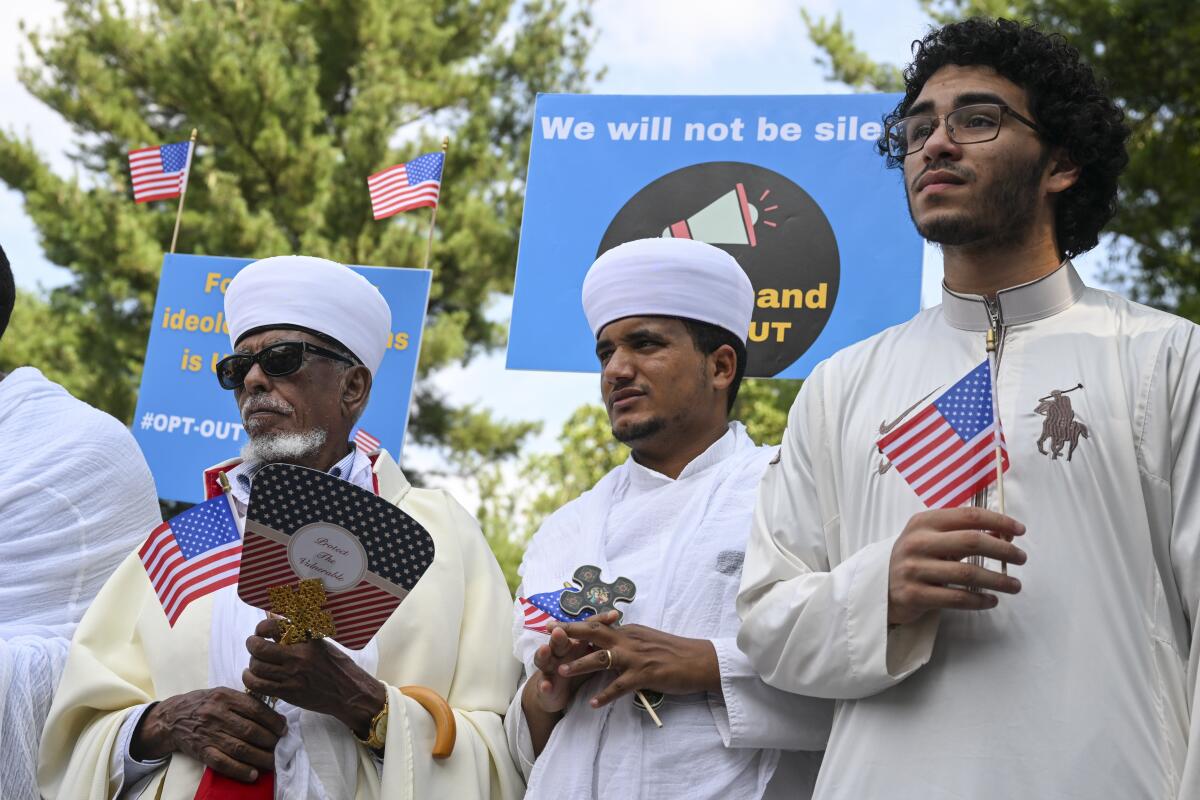Three men, two wearing caps, hold small American flags.