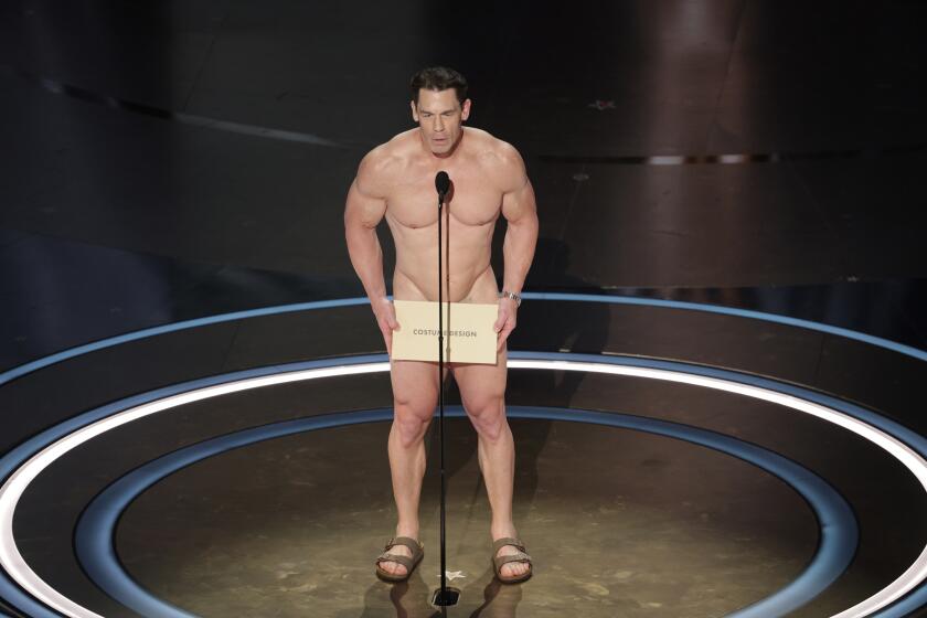 John Cena nude, holding a sandals and a big envelope in front of his groin