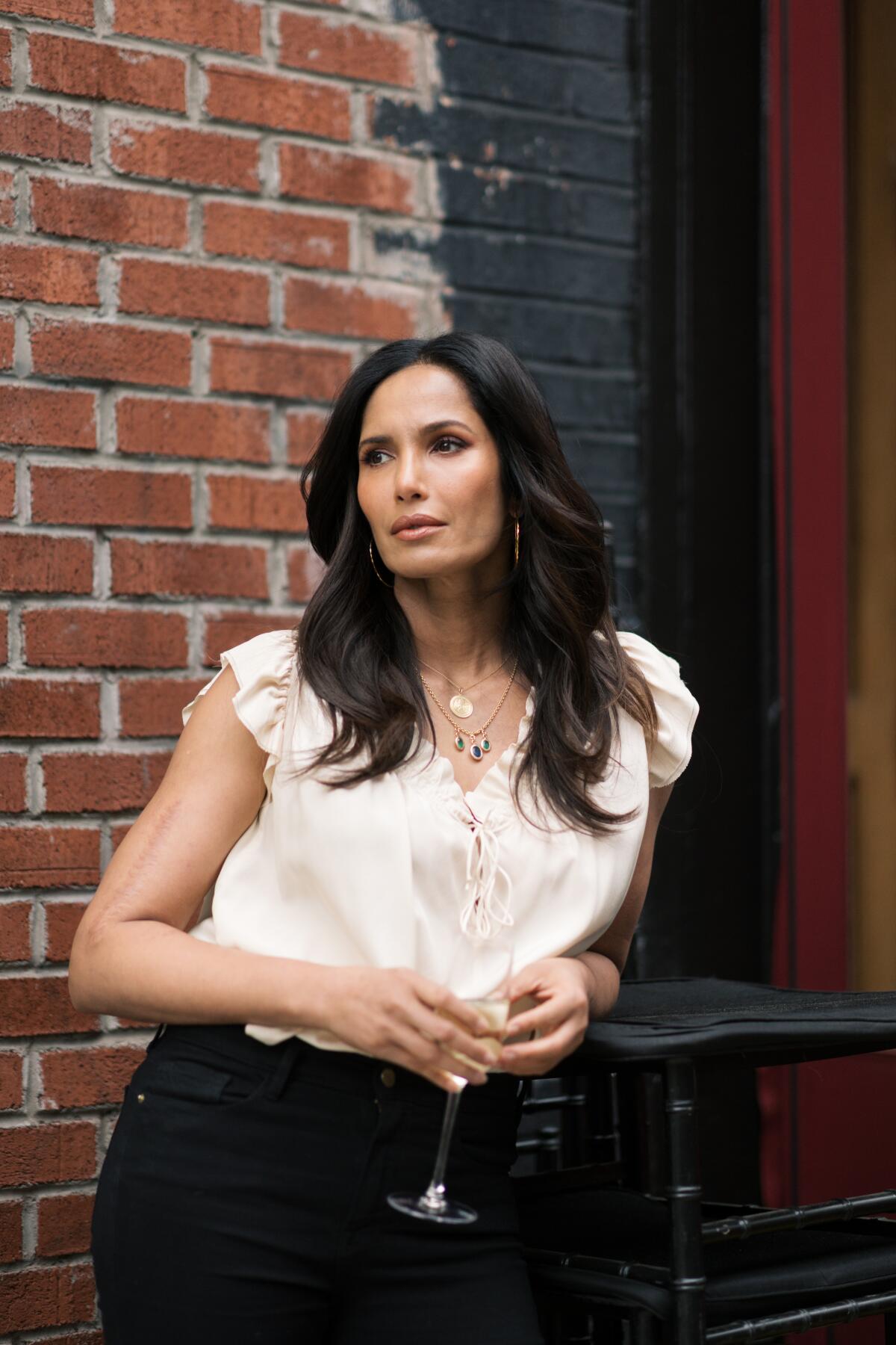 A woman holds a glass of wine against a brick wall.