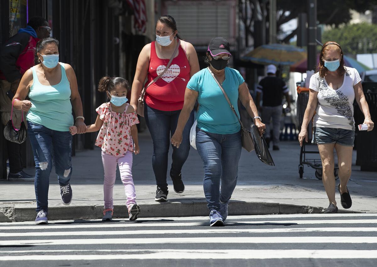 Masked pedestrians cross the street at 6th Street and Broadway in downtown Los Angeles.