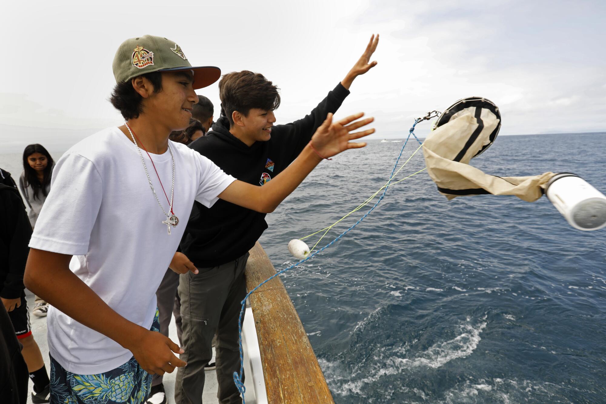 Two boys throw a net off the side of a boat in the ocean.