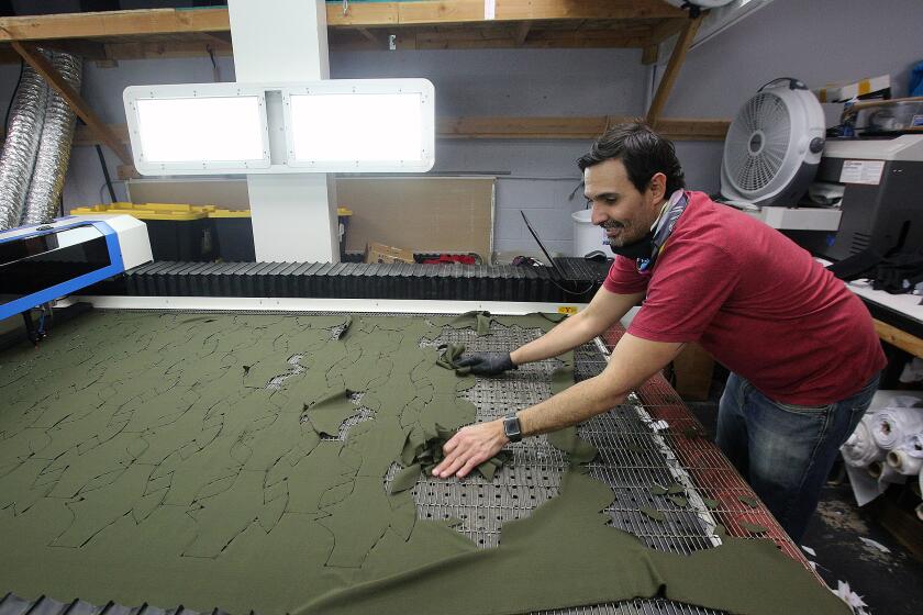 LiquidSky Sports owner Julio Ruiz uses his hands to sweep up mask patterns that had just been laser cut at LiquidSky sports in Burbank on Tuesday, March 24, 2020. LiquidSky shifted manufacturing from sports apparel, particularly skydiving suits, to making uncertified N95 masks using a custom mask pattern, a modified A/C filter, and copper wiring for fit due to a shortage on all mask supplies. The masks are washable and available for $25 where an additional mask will be given to someone in need.