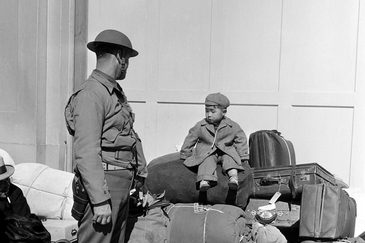 A boy sits on luggage as a solider looks at him