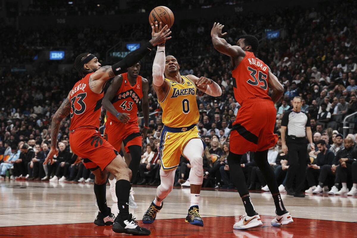 Lakers' Russell Westbrook drives between the Toronto Raptors' Gary Trent Jr., left, and Christian Koloko.
