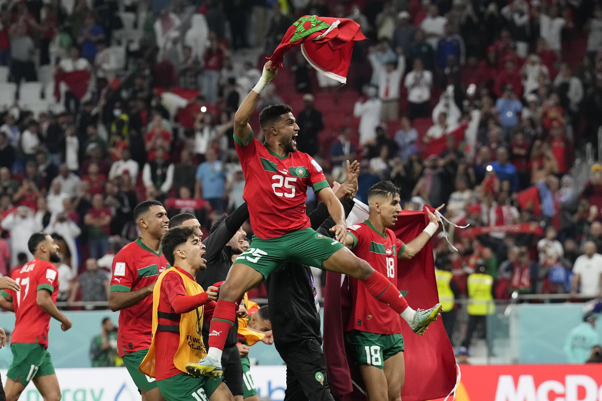 Morocco's Yahia Attiyat Allah jumps and waves his country's flag as he celebrates with teammates.