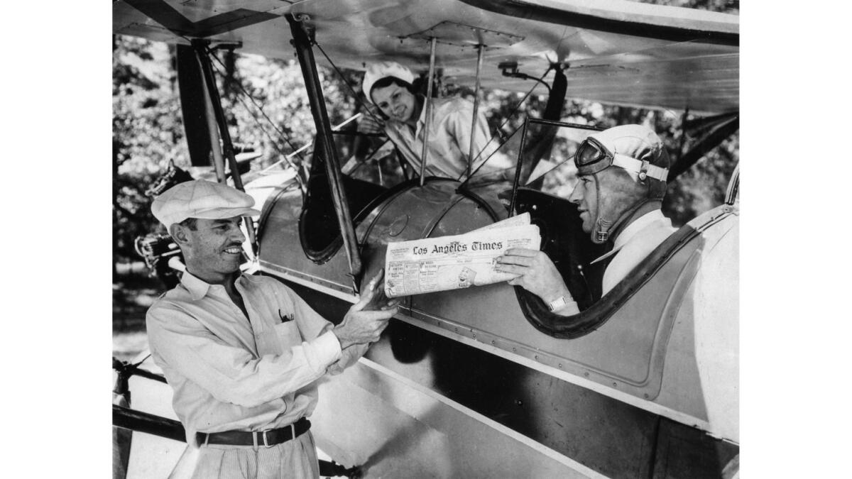Los Angeles pilot Allen Russel, right, hands a copy of the Los Angeles Times to W.R. Rohrer, manager of Meyers Land Co.