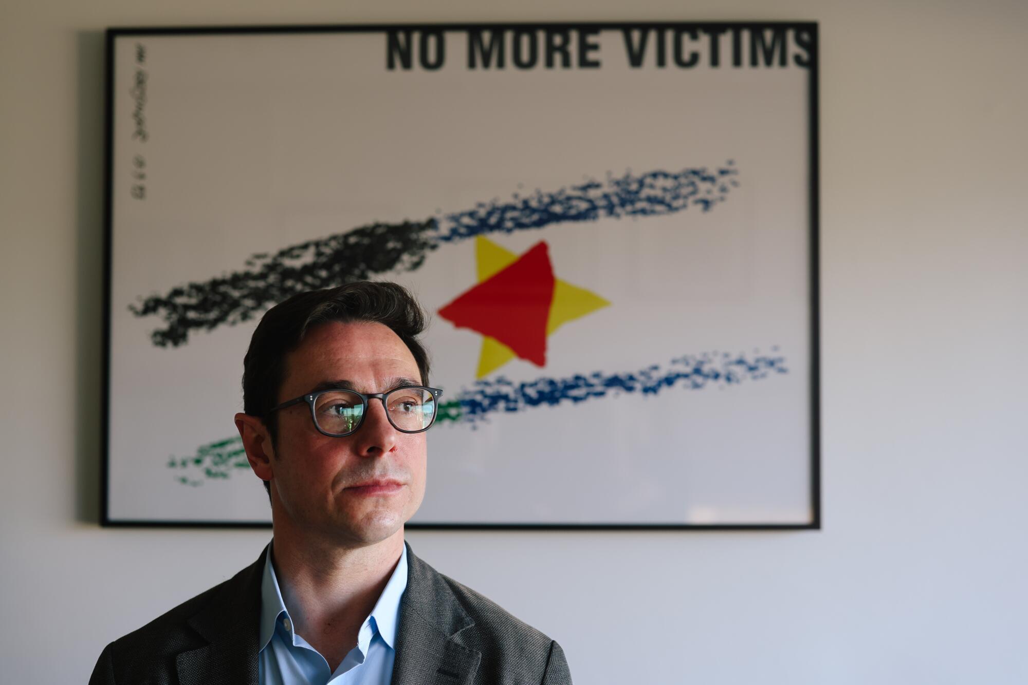 Dov Waxman poses in front of a framed poster that says, 'No More Victims'
