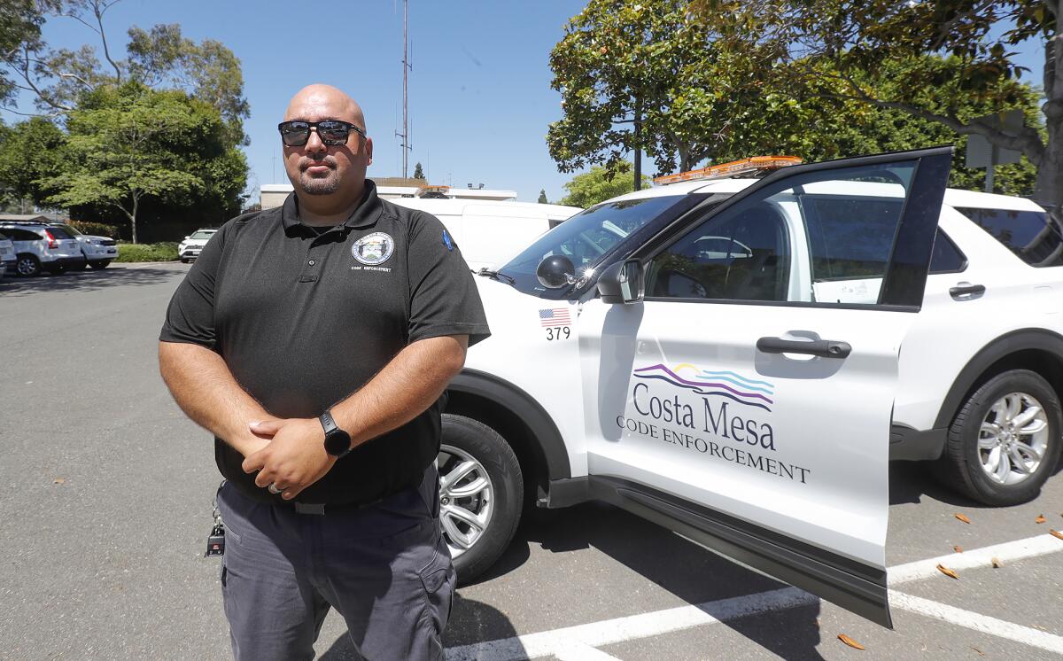Andy Godinez, a code enforcement officer with the city of Costa Mesa, stands with his city vehicle he drives daily.