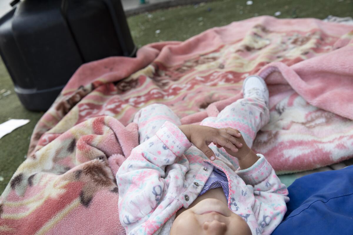 A baby lies on a blanket in a park