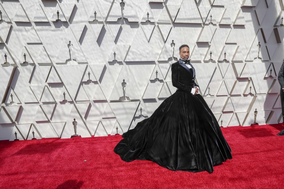 A man wearing a black dress with a long train on a red carpet