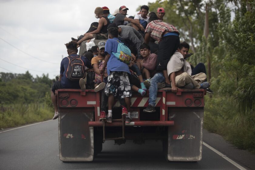Migrants ride on the back of a freight truck that slowed down to give them an opportunity to jump on in Rio Dulce, Guatemala, Friday, Oct. 2, 2020. A new caravan of about 2,000 migrants set out from neighboring Honduras in hopes of reaching the United States. (AP Photo/Moises Castillo)
