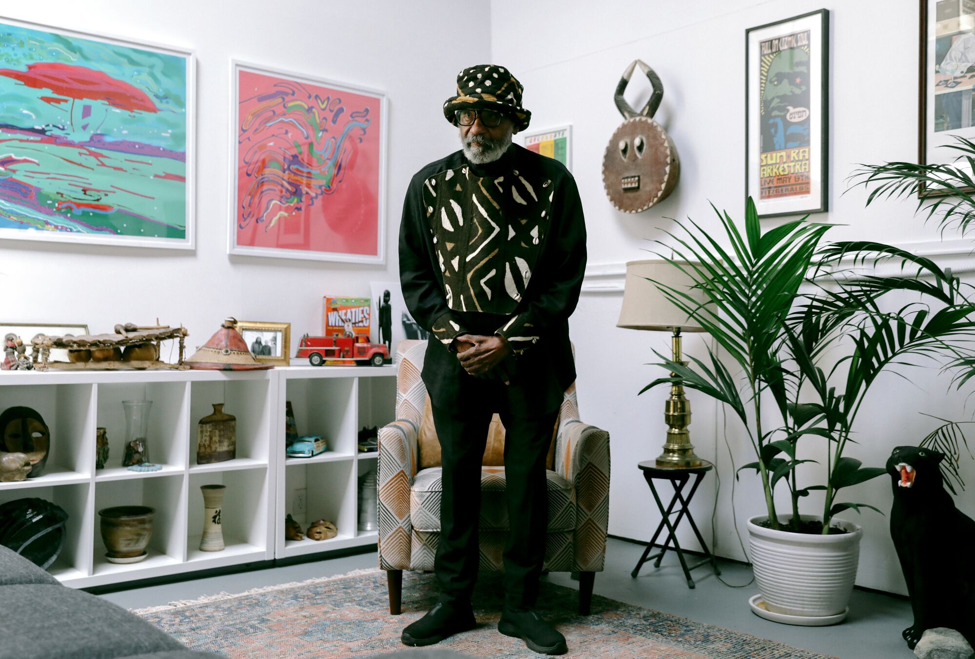 Ulysses Jenkins, dressed in a shirt with an African pattern, stands between two abstract works and an African mask.