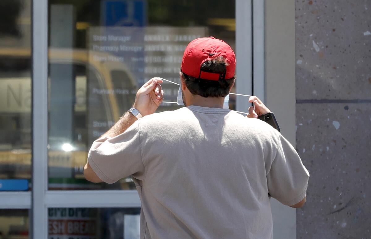 A shopper puts on a face covering before walking into a store in Costa Mesa on Monday.