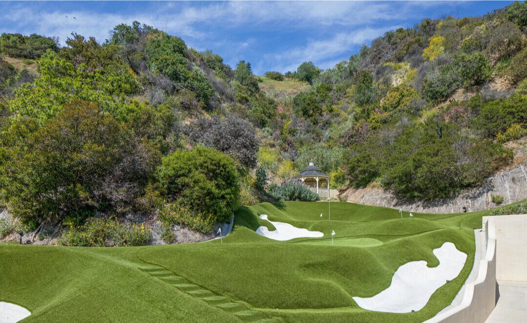 The golf course with foliage-covered hills behind it.