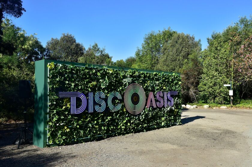 A sign on a backdrop of greenery reads DiscOasis with the "O" styled as a vinyl record