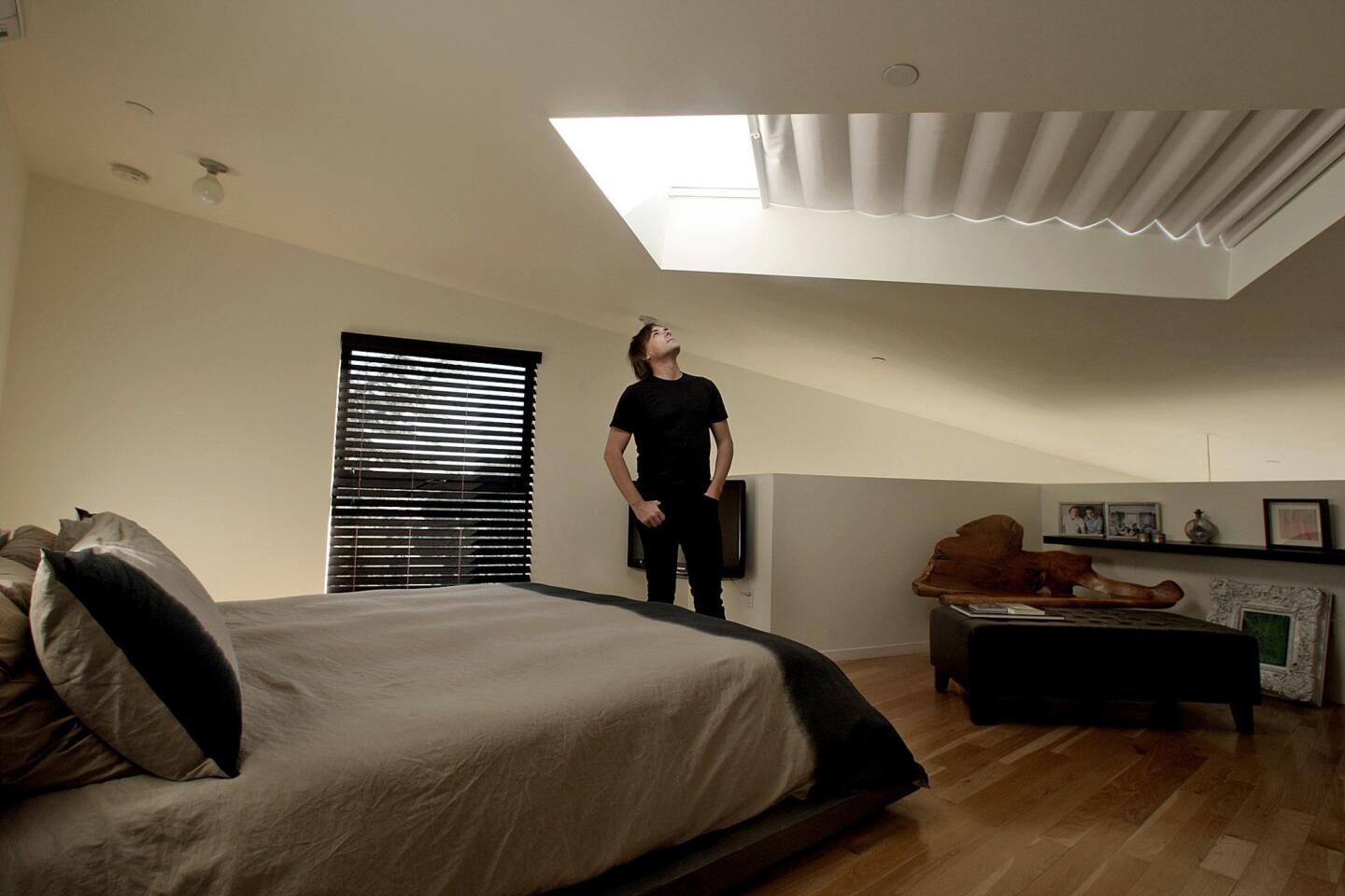 Architect Simon Storey stands in the bedroom he designed for a Mount Washington home; the space features a large skylight that frames views of the treetops and partial walls that continue the free-flowing sightlines. [ Full gallery ]