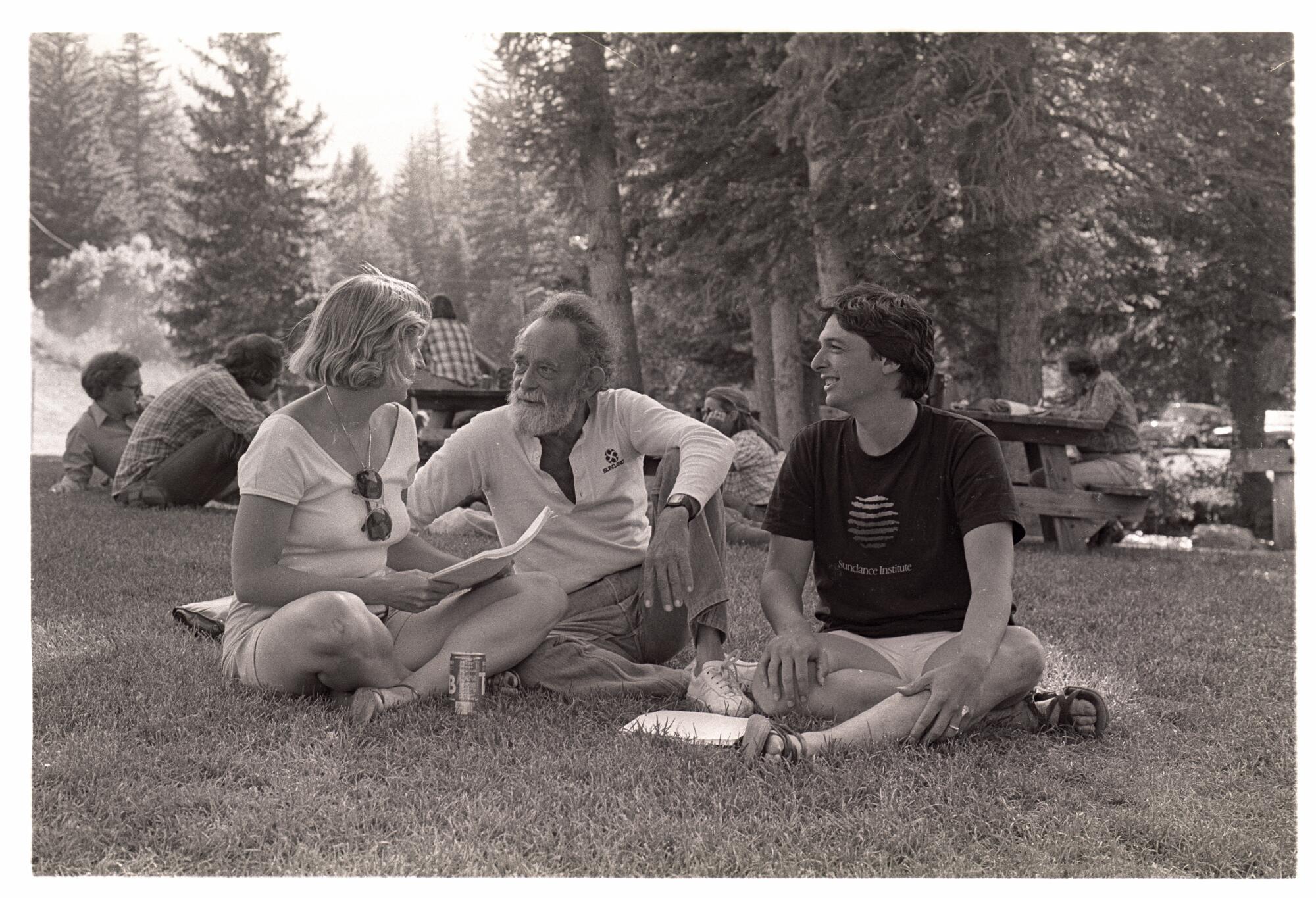 A black-and-white photo of a woman, left and two women sitting in the grass