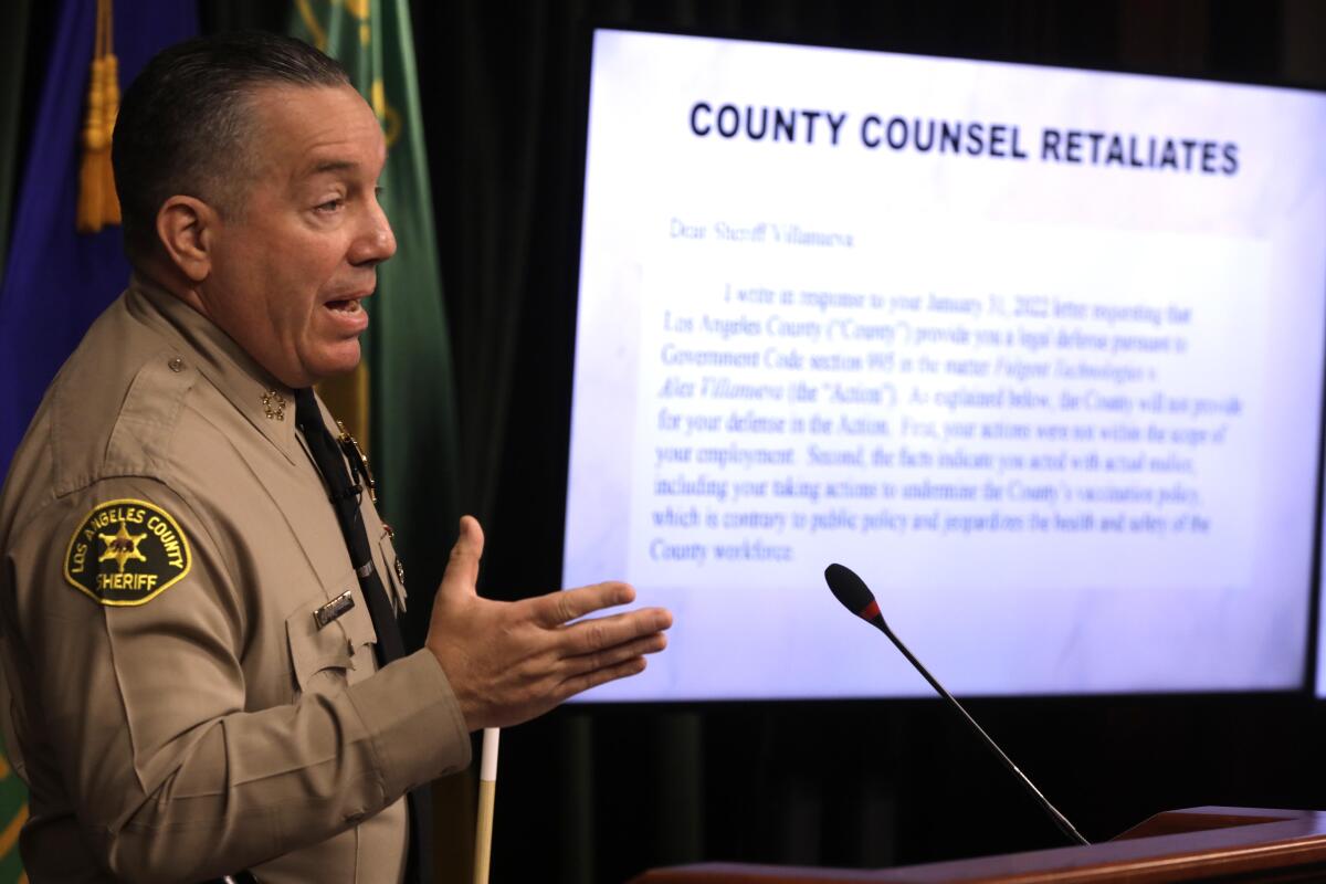 Alex Villanueva in front of a screen that reads, "County counsel retaliates."