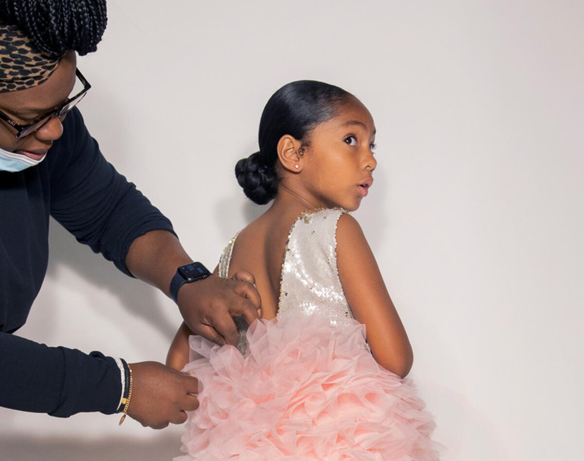Michelle Youngblood, owner of Brooklynn & Blake, fits one of her designer dresses, called Modern Ballerina, on Ava Marie, 8.