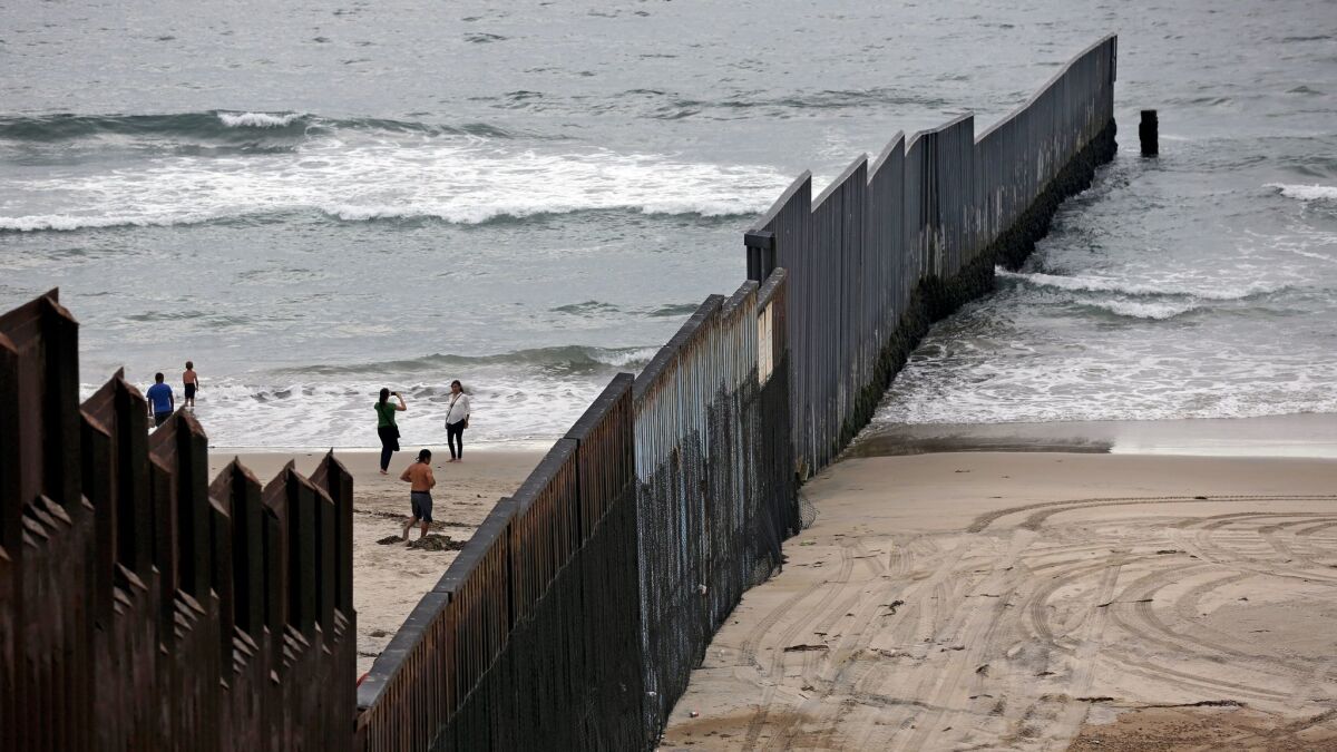 People take photos at the beach in Tijuana, left, while the water's edge at Border Field State Park in San Diego, right, is empty.