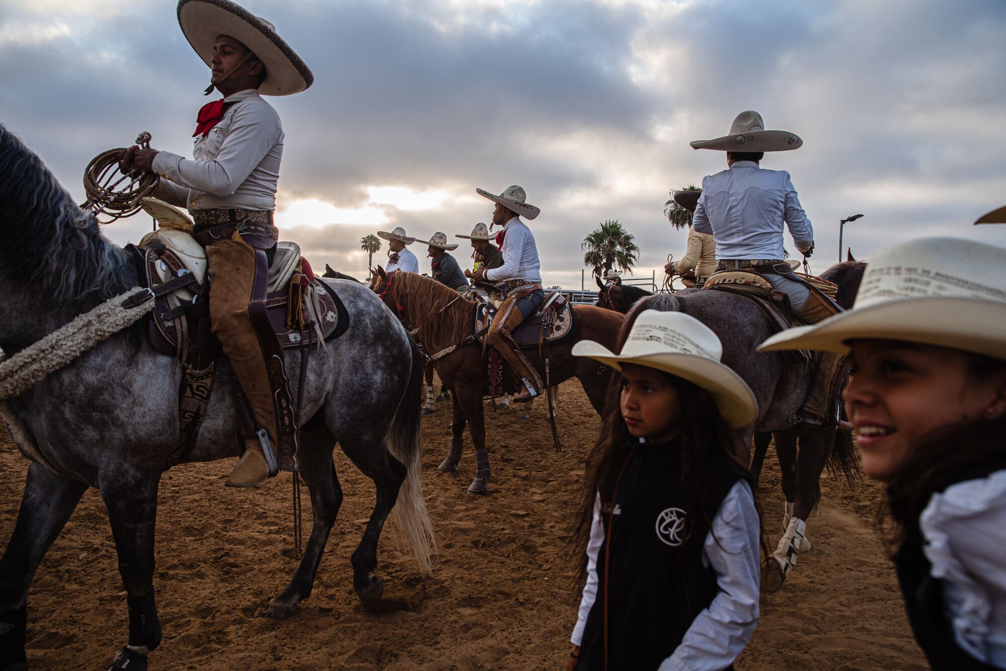 Men in traditional charro attire ride horses as children in cowboy hats watch at Rancho La Laguna in San Ysidro.