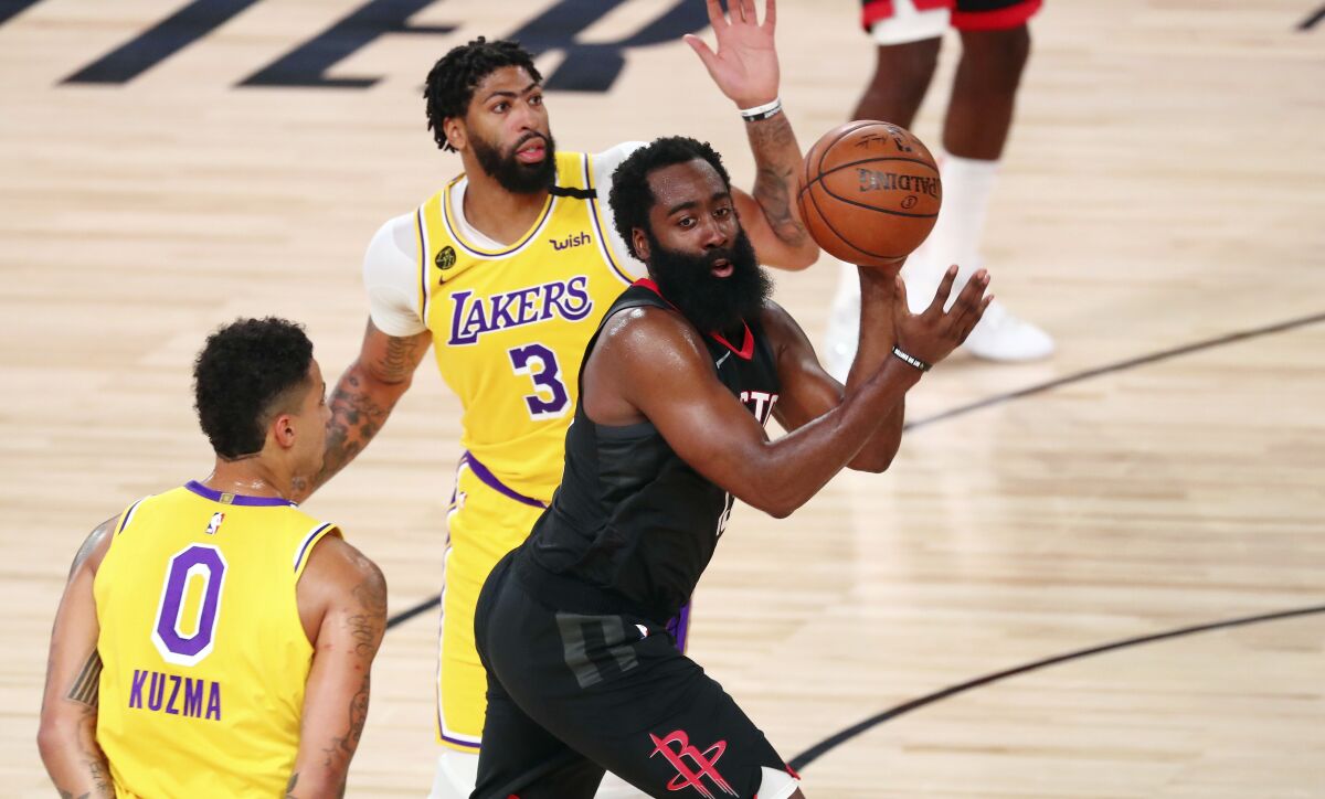 Rockets guard James Harden passes the ball between Lakers forward Kyle Kuzma and forward Anthony Davis.
