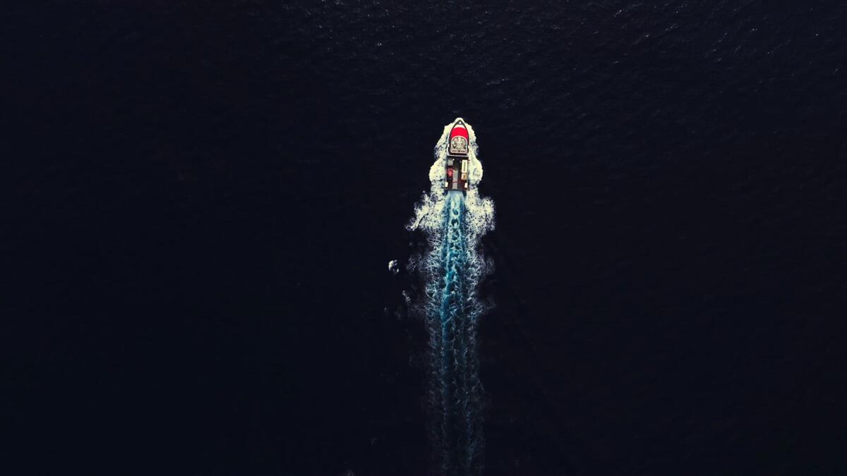 An aerial view of a boat moving, seen against a dark ocean.