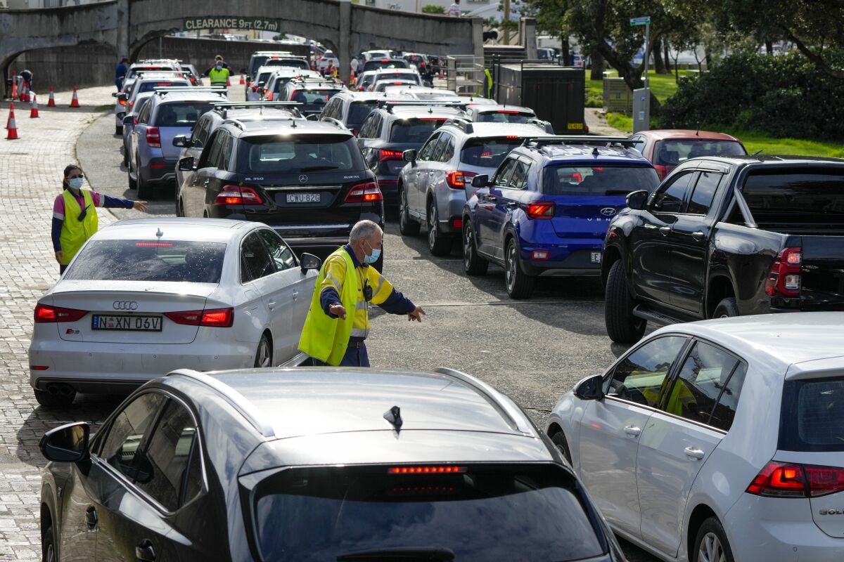 Traffic marshalls direct cars at a drive-through COVID-19 testing clinic at Bondi Beach in Sydney, Australia, Saturday, Jan. 8, 2022. Australia's most populous state has reinstated some restrictions and suspended elective surgeries as COVID-19 cases surged to another record. (AP Photo/Mark Baker)