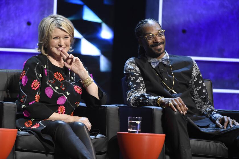 Martha Stewart in floral blouse and Snoop Dogg in vest and paisley bandana shirt smile while sitting on leather chairs.