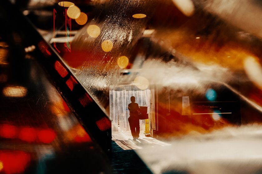 A double exposure of a man carrying boxes with the lights of Grand Central Market in downtown Los Angeles. / Bethany Mollenkof for the Los Angeles Times