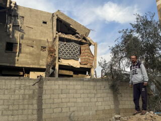 A man walks by a stone wall near a badly damaged house.