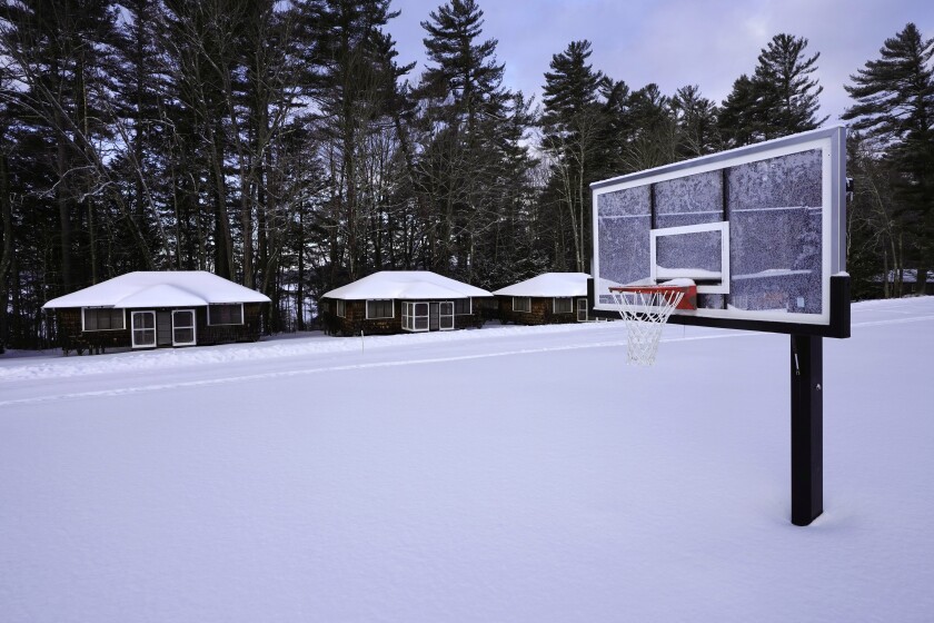 Snow covers a basketball court at Camp Fernwood, a summer camp for girls, Saturday, Feb. 20, 2021, in Poland, Maine. Camp directors across the country are feeling more confident about reopening this summer after a pandemic hiatus in 2020, but in some states they are still awaiting guidelines. (AP Photo/Robert F. Bukaty)