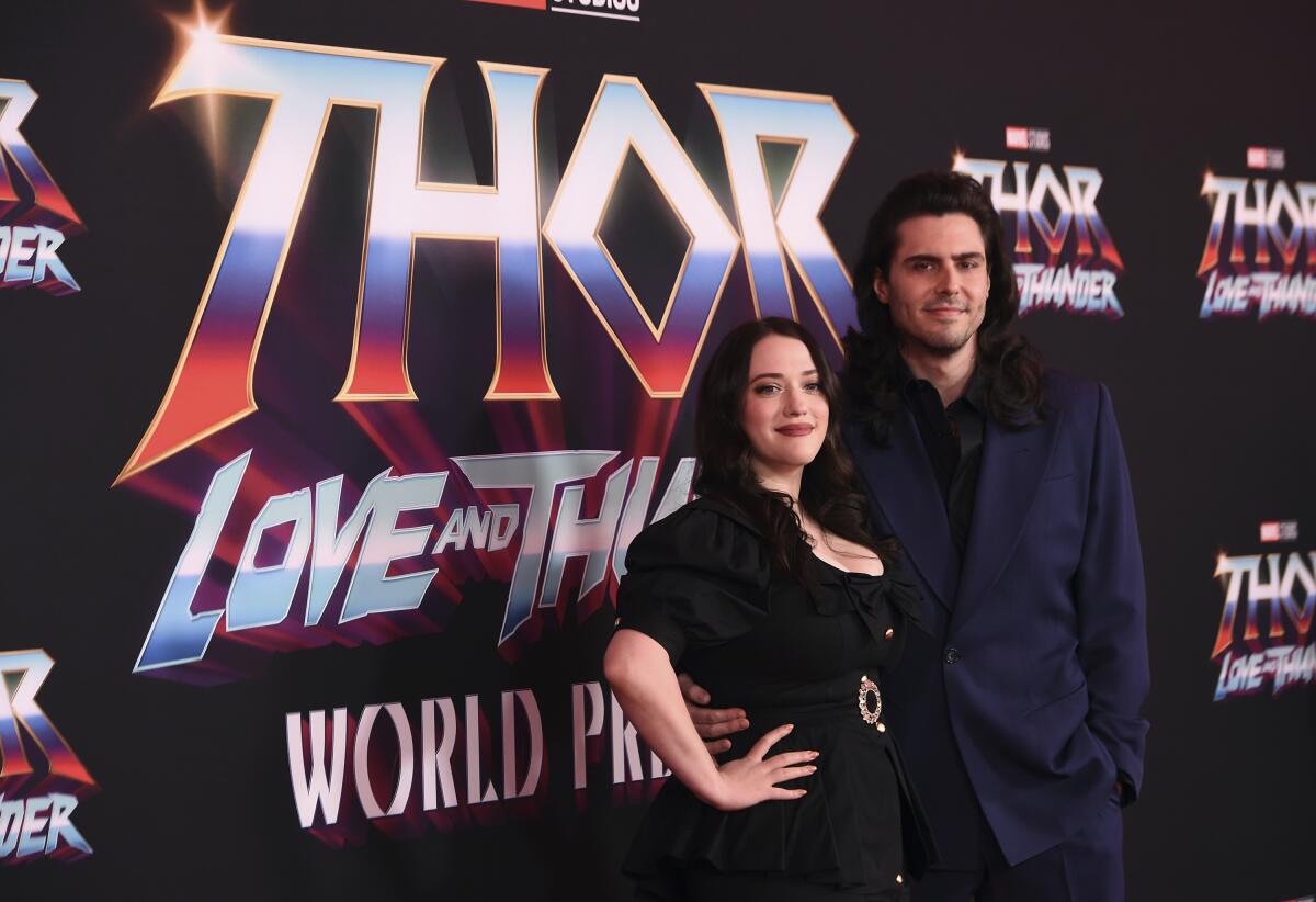 Kat Dennings, left, wears a black dress and Andrew W.K. wears a blue suit as the two pose in front of a "Thor" backdrop