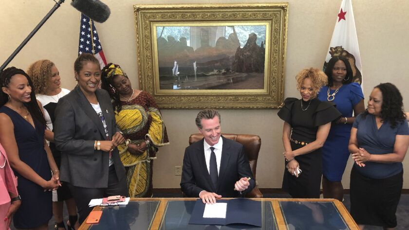 Gov. Gavin Newsom, center, signs legislation by state Sen. Holly Mitchell of Los Angeles, third from left, that bans workplace and school discrimination against black people for wearing natural hairstyles, including locks and braids.