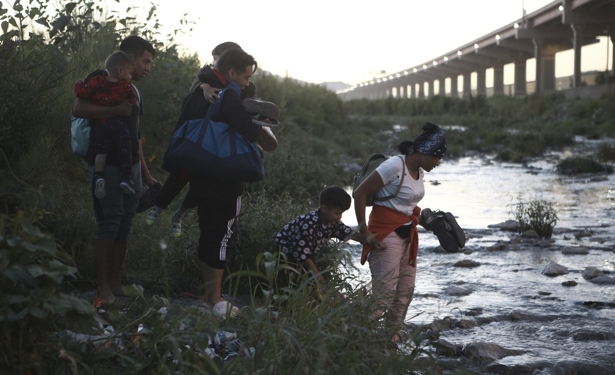 People with children stand at the edge of a river. 