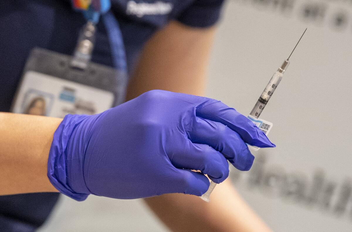 A close shot of a medical worker's hand in a purple glove, holding a loaded syringe