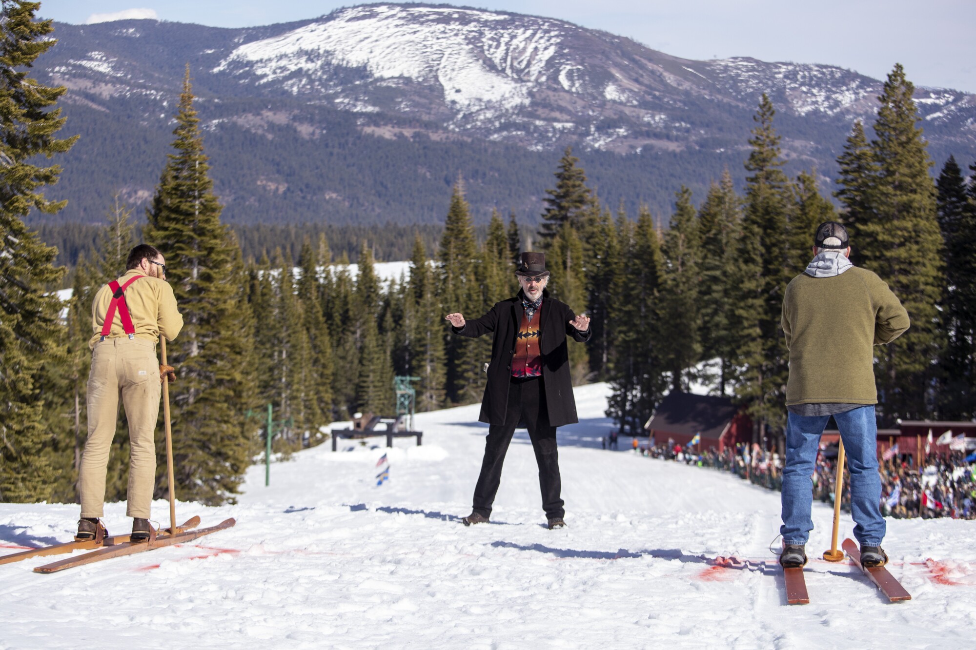 Two racers on skis, with a starter in a top hat between them