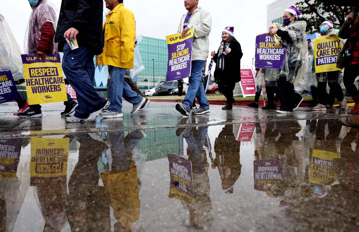 Healthcare workers are reflected in a puddle as they carry picket signs outside St. Francis Medical Center in Lynwood.