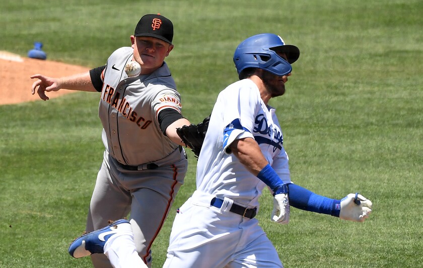 Dodgers' Cody Bellinger reaches first base as Giants pitcher Logan Webb drops the ball while trying to tag him.