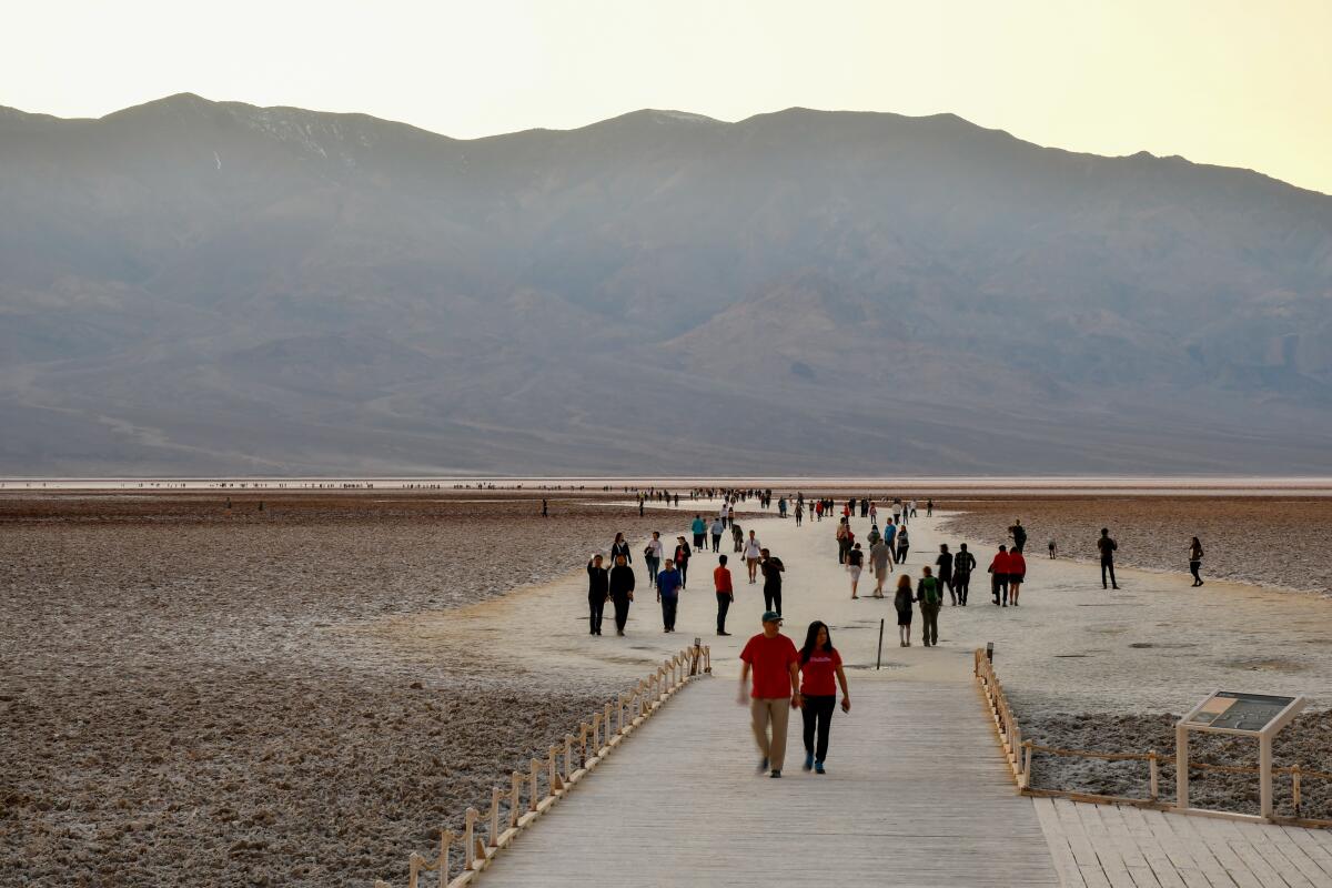 People walk outdoors near hills in Badwater in Death Valley National Park.