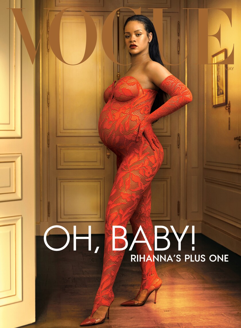 A pregnant woman stands in a lace bodysuit and high heels