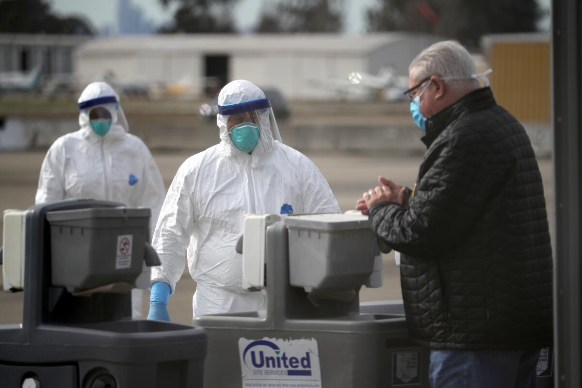 Medical workers watch a passenger from the Grand Princess cruise ship as he washes his hands before boarding a charter plane at Oakland International Airport on Tuesday in Oakland.