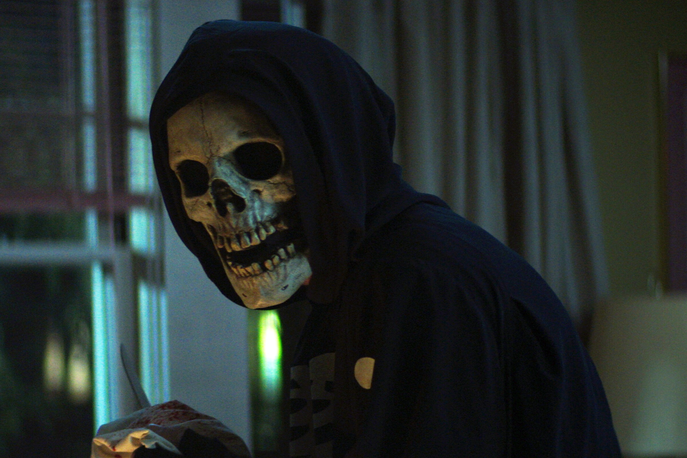 A hooded figure in a skull mask in a living room